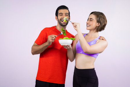 Full body length gaiety shot athletic and sporty young couple with healthy vegan food in standing posture on isolated background. Healthy active and body care by vegetarian lifestyle.の写真素材