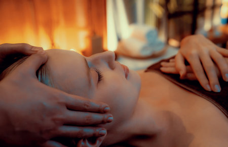 Caucasian woman enjoying relaxing anti-stress head massage and pampering facial beauty skin recreation leisure in warm candle lighting ambient salon spa in luxury resort or hotel. Quiescentの写真素材