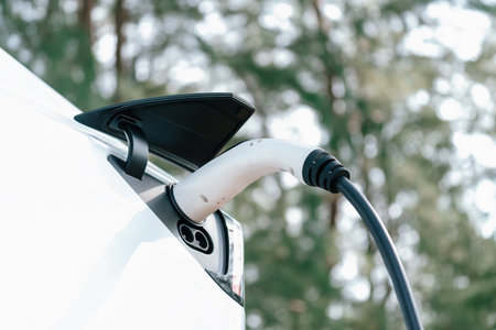 Closeup EV charger handle plugged in or connect to electric car, recharging EV car battery with...