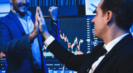 Cheerful two stock exchange traders giving high five for digital currency achievement on dynamic...