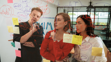 Creative business team brainstorming and sharing marketing idea about start up project by writing down on colorful sticky note at glass board modern meeting room. Working together. Immaculate.の写真素材