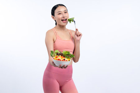Young sporty Asian woman in sportswear holding salad bowl fill with vibrant of fruit and vegetable. Natural youthful and fit body lifestyle with balance nutrition on isolated background. Vigorousの写真素材