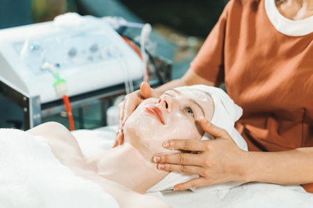 Portrait of beautiful caucasian woman having facial massage with homemade facial mask while lies on spa bed surrounded by beauty electrical equipment and peaceful nature environment. Tranquility.の写真素材