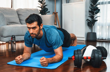 Athletic and sporty man doing plank on fitness mat during home body workout exercise session for fit...