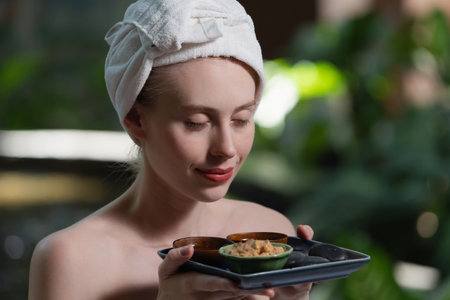 Portrait of beautiful caucasian woman in white towel holds the tray which contained the bowl of herbal scrub and spa rock surrounded by calm and relaxing nature. Side view. Tranquility.の写真素材