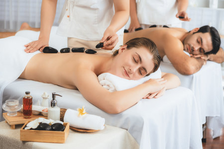 Hot stone massage at spa salon in luxury resort with day light serenity ambient, blissful couple customer enjoying spa basalt stone massage glide over body with soothing warmth. Quiescentの写真素材