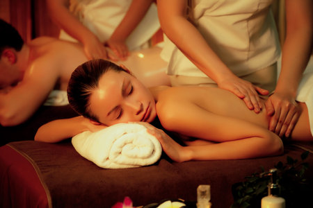 Caucasian couple customer enjoying relaxing anti-stress spa massage and pampering with beauty skin recreation leisure in warm candle lighting ambient salon spa at luxury resort or hotel. Quiescentの写真素材