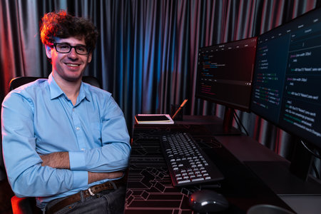 Profile of smiling IT developer sitting against software development information on screen, looking...