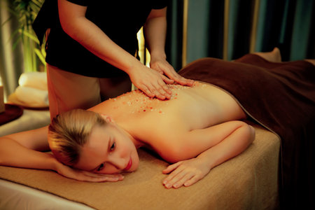 Woman customer having exfoliation treatment in luxury spa salon with warmth candle light ambient. Salt scrub beauty treatment in Health spa body scrub. Quiescentの写真素材