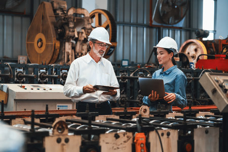 Factory engineer manager with assistant using laptop to conduct inspection of steel industrial machine, exemplifying leadership as machinery engineering inspection supervisor in metalwork manufacture.の写真素材