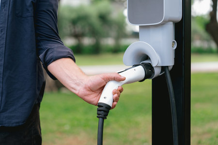 Man recharge EV electric vehicles battery from EV charging station in outdoor green city park...