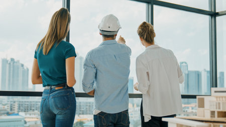 Group of caucasian diverse architect engineer pointing at skyscraper at day time. Skilled manager team looking at city or skyscraper while house model was placed on table. Back view. Traceryの写真素材