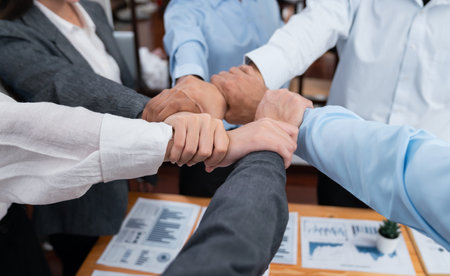 Diverse team of officer workers hold hands in circle, showing solidarity and teamwork in corporate office. Businesspeople form strong community built on integrity and collaboration. Concordの写真素材