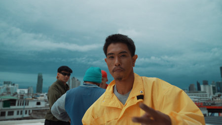 Hispanic hipster looking at camera at rooftop with city surrounded by multicultural friends. Street dancer dancing while smiling at camera. Active, energetic, caucasian. Outdoor sport 2024. Endeavor.の写真素材