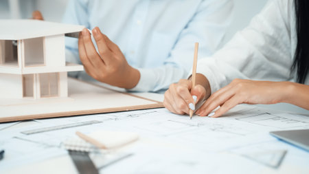 Professional engineer measures house model while skilled designer writes down in blueprint. Work...