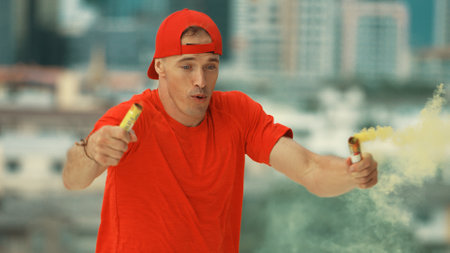 Portrait of skilled caucasian hipster hold yellow smoke flare on roof top at building. Group of break dance practicing performance with sky scrapper Blurring background. Outdoor sport 2024. Endeavor.の写真素材