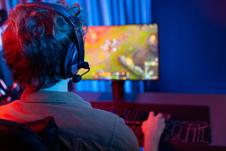Host channel of young gaming streamer playing fighting Moba at battle arena game with multiplays team, wearing headphone on pc monitor with back side image at neon digital light modern room. Gusher.の写真素材