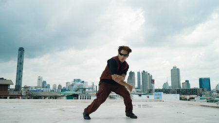 Motion shot of B-boy dance performance by professional street dancer at rooftop with sky scrapper,...