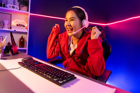 Host channel of smiling beautiful Asian girl streamer playing with raising fist up winning on Esport skilled team players wearing headphones pastel color, fighting online game at neon room. Stratagem.の写真素材