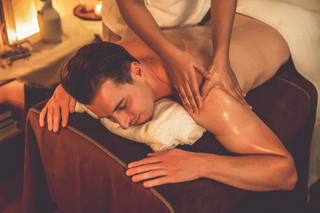 Caucasian man customer enjoying relaxing anti-stress spa massage and pampering with beauty skin recreation leisure in warm candle lighting ambient salon spa at luxury resort or hotel. Quiescentの写真素材