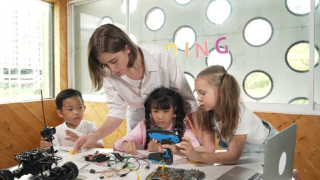 Teacher looking at children while diverse student looking at screen. Children excited in presentation while drawing or writing art books at table with toys and color pencil placed on table. Erudition.の写真素材