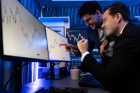 Cheerful two stock exchange traders raising fist up for digital currency achievement focusing on...