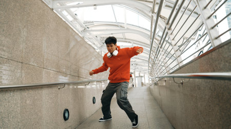 Skilled asian break dancer show b-boy step dance at narrow corridor. Professional energetic hipster moving to hip hop music and wearing headphone. Modern lifestyle. Outdoor sport 2024. Sprightly.の写真素材