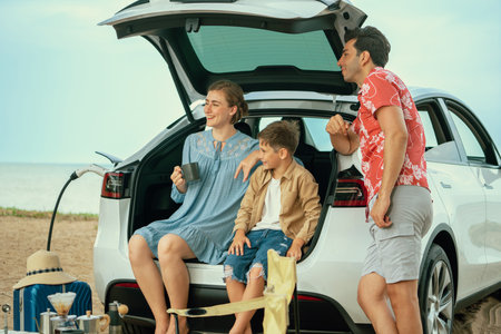 Family vacation trip traveling by the beach with electric car, happy family recharge EV car, enjoying outdoor camping coffee. Seascape travel and eco-friendly car for clean environment. Perpetualの写真素材