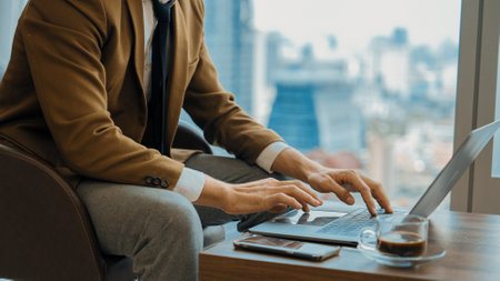 Businessman sitting on furniture working on laptop at ornamented corporate waiting area with cityscape background on the window. Business profession and strategic marketing plan for business success.の写真素材