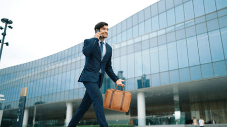 Smart business man using phone to talking while walking at building. Happy manager walking at street while talking on smart phone to discuss business plan or marketing strategy or working. Exultant.の写真素材
