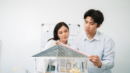 Professional young beautiful architect engineer using ruler and pencil measuring model roof length at modern office with blueprint hanged behind. Creative design and teamwork concept. Immaculate.の写真素材
