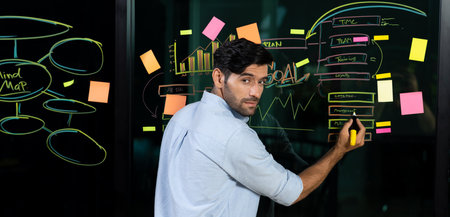 Portrait of skilled businessman writing marketing idea on glass wall with chart, mind map and sticky...