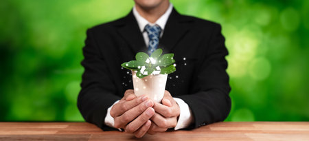 Businessman nurturing and holding plant with recycle symbol. Business commitment and investing in...