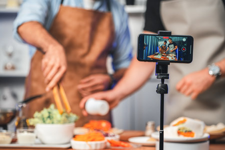 Cropped view of chef influencers presenting fresh salad roll on cooking step by step, streaming via smartphone on social media live channel, showing ingredients vegetable soft tortilla wrap. Sellable.の写真素材