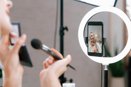 Rear view young woman making beauty and cosmetic tutorial video content for social media. Beauty blogger showing how to apply beauty care to audience or follower on camera screen. Blitheの写真素材