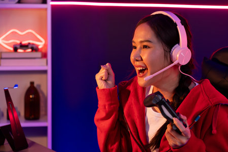Host channel of smiling beautiful Asian girl streamer with joystick playing with raising fist up...