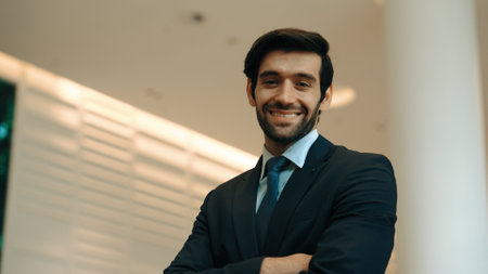 Professional business man standing with arm folded at modern mall. Smiling caucasian investor looking at camera with confident while crossing arms at hall with blurring background. Portrait. Exultant.の写真素材