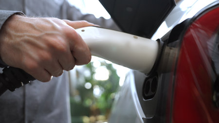 Young man recharge EV electric car in green sustainable city outdoor summer garden as lifestyle of young people in urban sustainability green clean rechargeable energy of electric vehicle innardsの写真素材