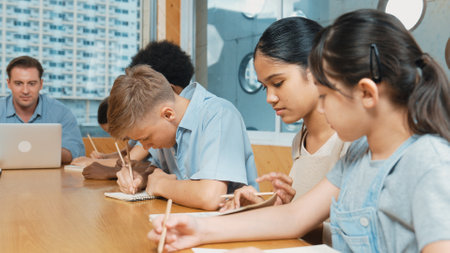 Caucasian teacher and multicultural students clapping hand or putting the hand in the air together to celebrate for successful project with laptop and equipment placed on table in class. Edification.の写真素材
