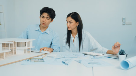 Professional male engineer measure house model by using ruler while beautiful cooperative coworker working together by using laptop to analysis data. Creative design and teamwork. Closeup. Immaculate.の写真素材