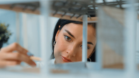 Closeup of young beautiful caucasian skilled architect engineer focusing on checking the house model...