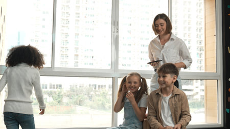 Diverse children playing musical chairs games while young smart beautiful teacher turn off music....