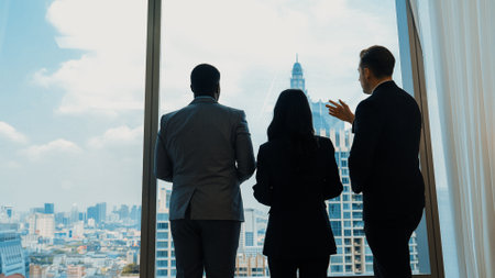 Back view diverse team of ambitious business people standing in ornamented office gazing out window...