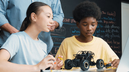 Caucasian teacher looking at laptop screen while explain car model system at blackboard with coding or programing code written. Happy diverse student learning about robotic construction. Edification.の写真素材