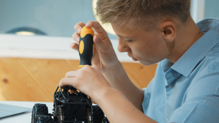Close up of young student tighten the nut by using screwdriver. Caucasian teenager repairing or fixing car model while inspect robotic machine construction at STEM technology class. Edification.の写真素材