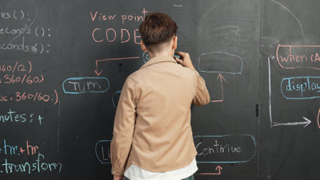 Back view of smart boy writing engineering prompt on blackboard. Attractive happy student planing a...