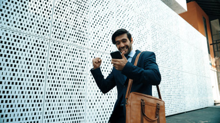 Happy smart business man celebrate for getting promotion or receive good news while walking at street. Skilled project manager or leader express feeling of overjoy at architectural building. Exultantの写真素材