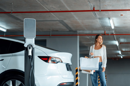 Young woman travel with EV electric car to shopping center parking lot charging in downtown city showing urban sustainability lifestyle by green clean rechargeable energy of electric vehicle innardsの写真素材