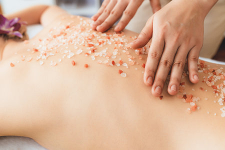 Closeup woman customer having exfoliation treatment in luxury spa salon with warmth candle light ambient. Salt scrub beauty treatment in health spa body scrub. Quiescentの写真素材