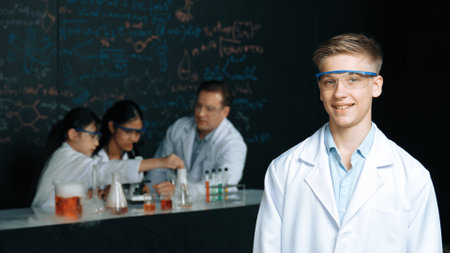Smart student looking at camera while diverse group doing experiment. Attractive academic boy standing at blackboard with biological theory while people working by using chemical liquid. Edification.の写真素材